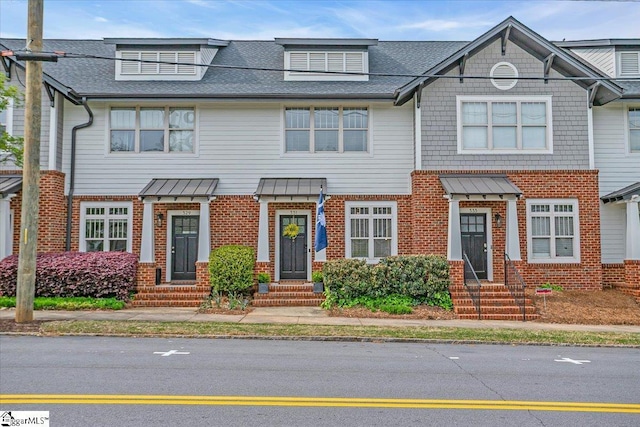view of property featuring brick siding, a standing seam roof, a shingled roof, and entry steps