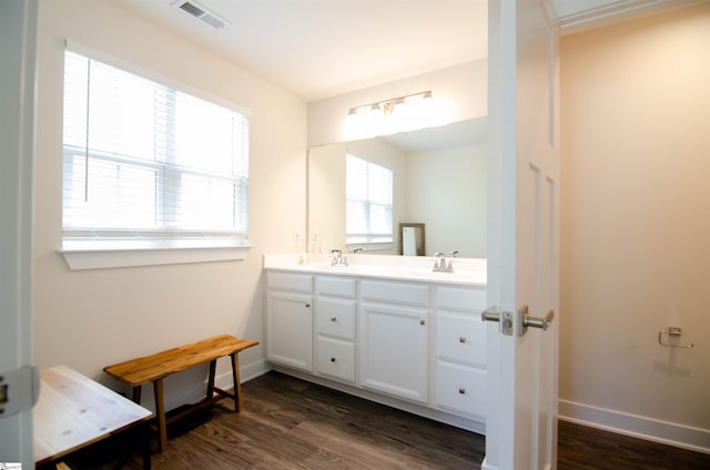 bathroom with a sink, double vanity, baseboards, visible vents, and wood finished floors