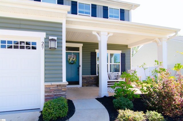 entrance to property with a garage, stone siding, and covered porch