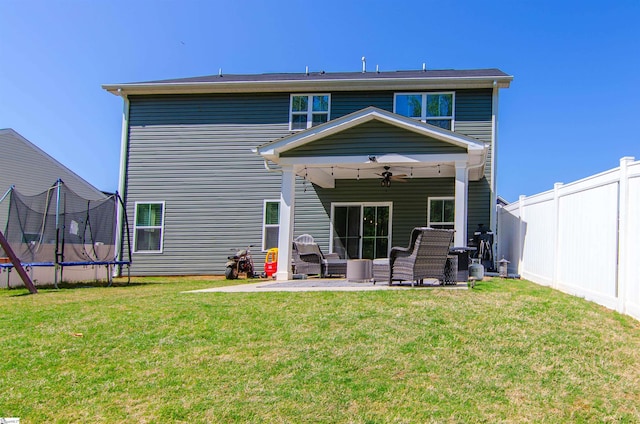 back of house with a trampoline, a ceiling fan, a fenced backyard, a yard, and a patio