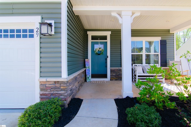 doorway to property featuring a garage, stone siding, and covered porch