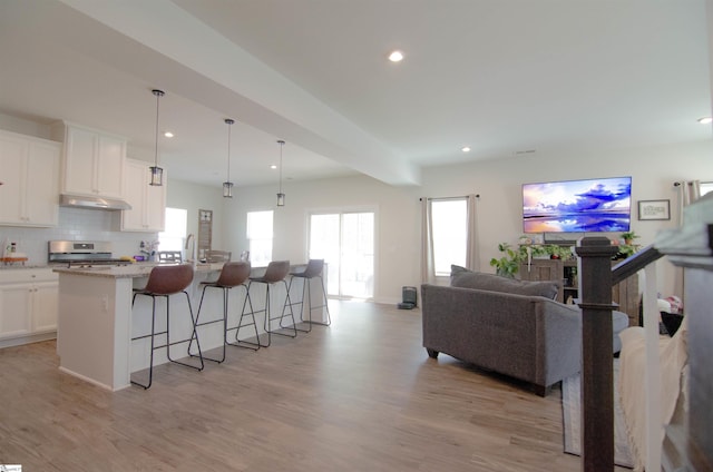 kitchen with stainless steel range, open floor plan, a kitchen bar, under cabinet range hood, and an island with sink