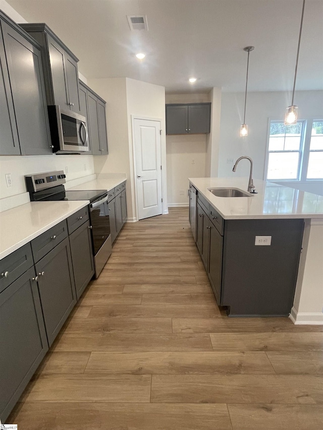 kitchen with a kitchen island with sink, light wood-style flooring, a sink, and appliances with stainless steel finishes