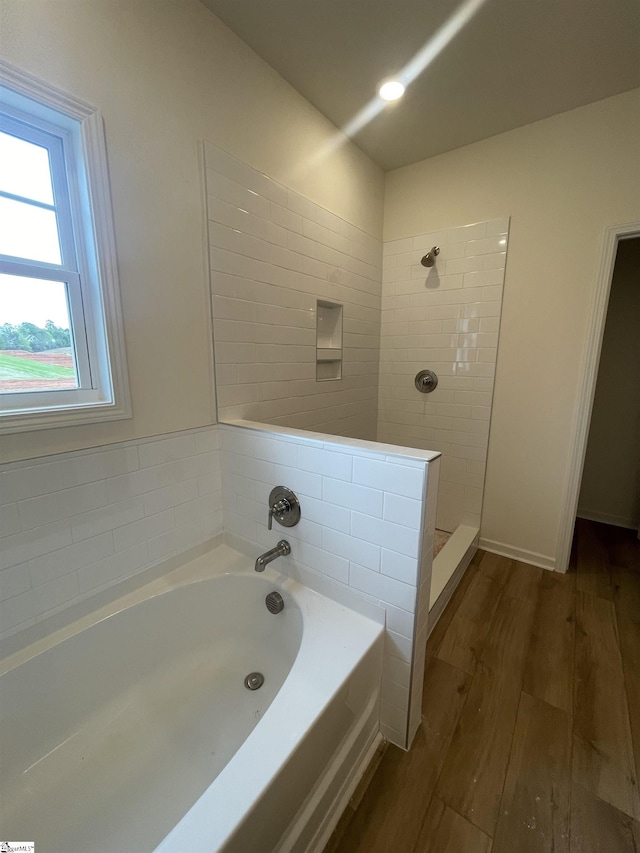 bathroom featuring a bath, wood finished floors, and tiled shower