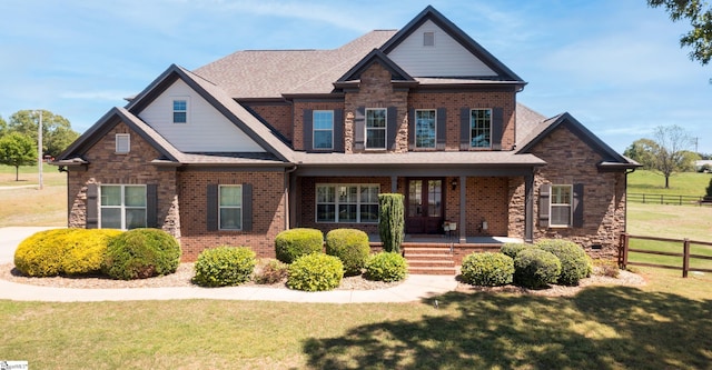 craftsman house with a porch, fence, a front yard, and brick siding