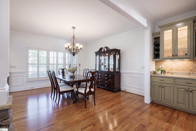 dining area featuring light wood finished floors, an inviting chandelier, ornamental molding, a decorative wall, and wainscoting