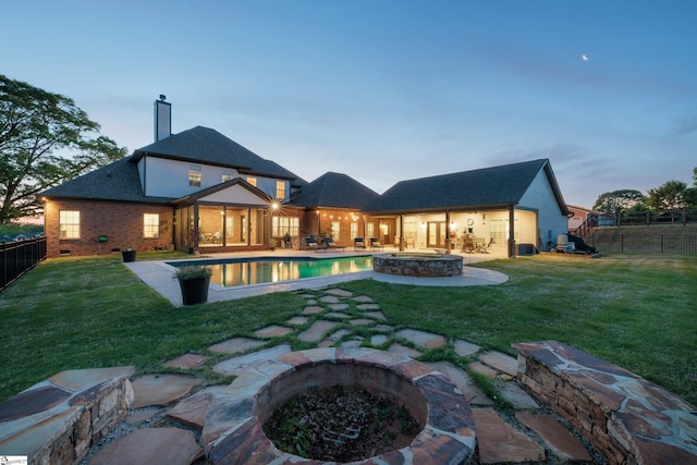back of property at dusk featuring a chimney, a fenced backyard, a yard, a patio area, and an outdoor fire pit