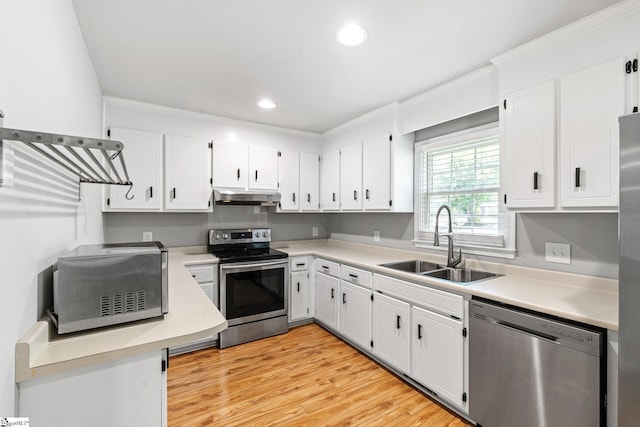 kitchen featuring a sink, under cabinet range hood, stainless steel appliances, light countertops, and ornamental molding