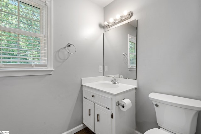 half bathroom with baseboards, vanity, a wealth of natural light, and toilet