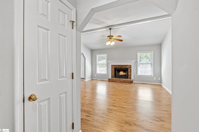 unfurnished living room with a fireplace, light wood-style floors, a ceiling fan, and baseboards