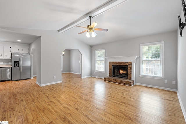 unfurnished living room with arched walkways, light wood-style flooring, a healthy amount of sunlight, and a ceiling fan