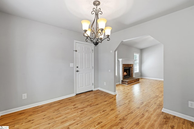 unfurnished dining area featuring baseboards, a notable chandelier, a brick fireplace, and light wood-style flooring