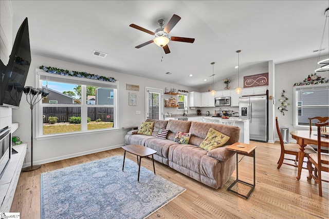 living area featuring a ceiling fan, light wood-style floors, baseboards, lofted ceiling, and visible vents