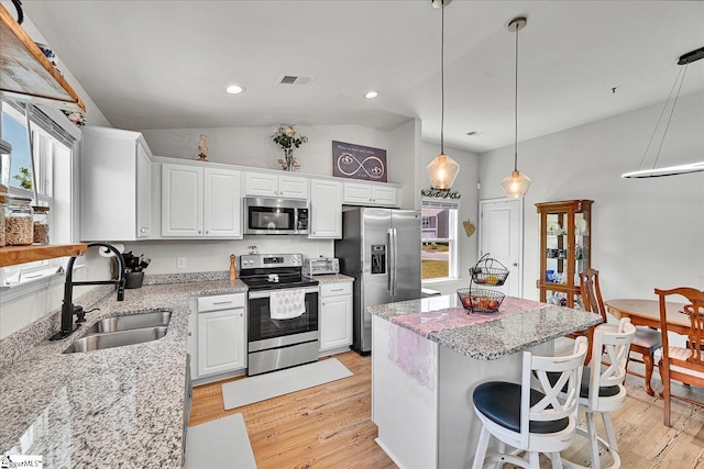 kitchen with light wood finished floors, vaulted ceiling, a sink, a kitchen island, and appliances with stainless steel finishes
