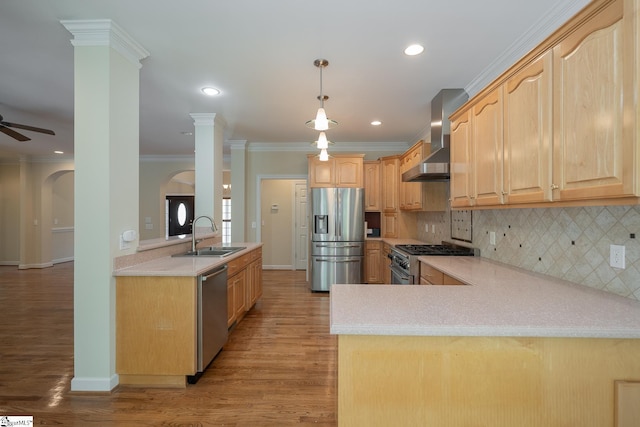 kitchen with wall chimney exhaust hood, stainless steel appliances, a peninsula, light brown cabinetry, and a sink