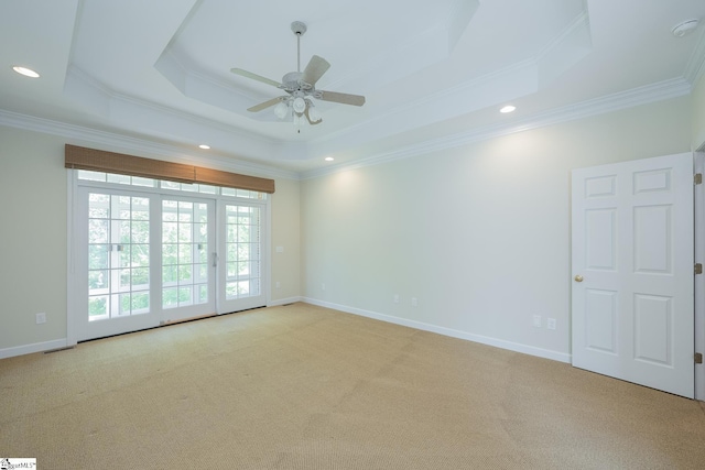 empty room with a tray ceiling, a ceiling fan, light carpet, crown molding, and baseboards
