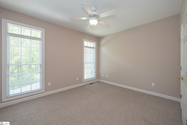 carpeted spare room with a healthy amount of sunlight, a ceiling fan, baseboards, and visible vents