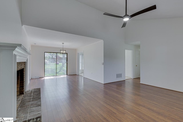 unfurnished living room featuring a towering ceiling, wood finished floors, visible vents, a fireplace, and ceiling fan with notable chandelier