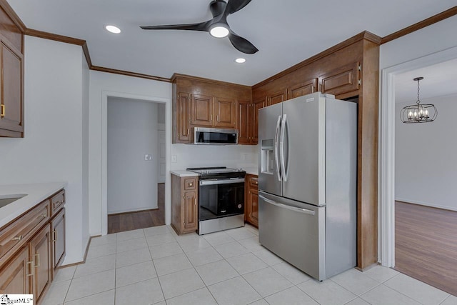 kitchen featuring stainless steel appliances, light countertops, ornamental molding, light tile patterned floors, and ceiling fan with notable chandelier