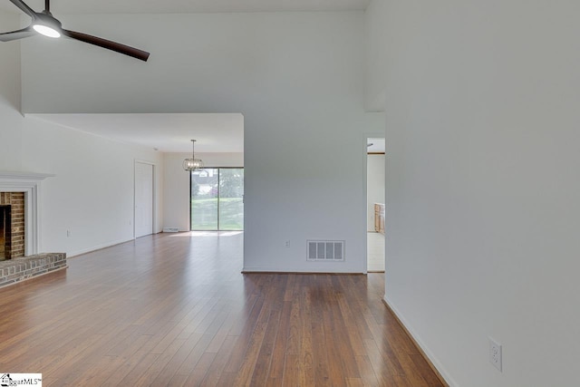 unfurnished living room with ceiling fan with notable chandelier, a fireplace, dark wood finished floors, baseboards, and visible vents