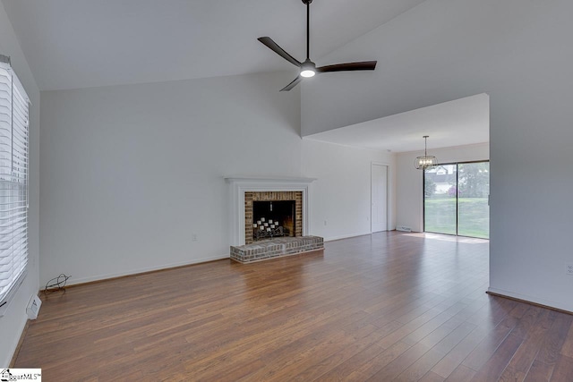 unfurnished living room featuring wood finished floors, baseboards, a fireplace, high vaulted ceiling, and ceiling fan with notable chandelier