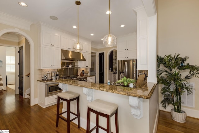 kitchen featuring arched walkways, under cabinet range hood, stainless steel appliances, tasteful backsplash, and ornamental molding