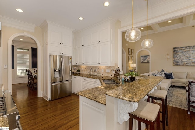 kitchen featuring appliances with stainless steel finishes, arched walkways, dark wood-style floors, a peninsula, and a sink