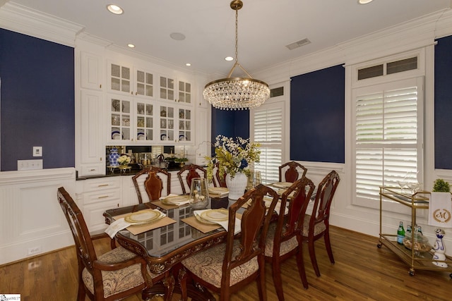 dining space with a chandelier, ornamental molding, a decorative wall, a wainscoted wall, and wood finished floors