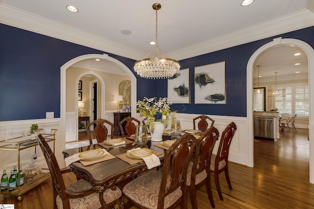 dining space with a chandelier, wainscoting, arched walkways, a decorative wall, and wood finished floors
