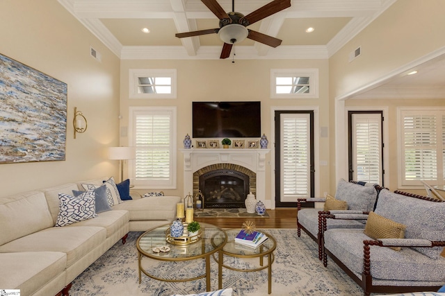 living area with a ceiling fan, coffered ceiling, beam ceiling, ornamental molding, and a fireplace
