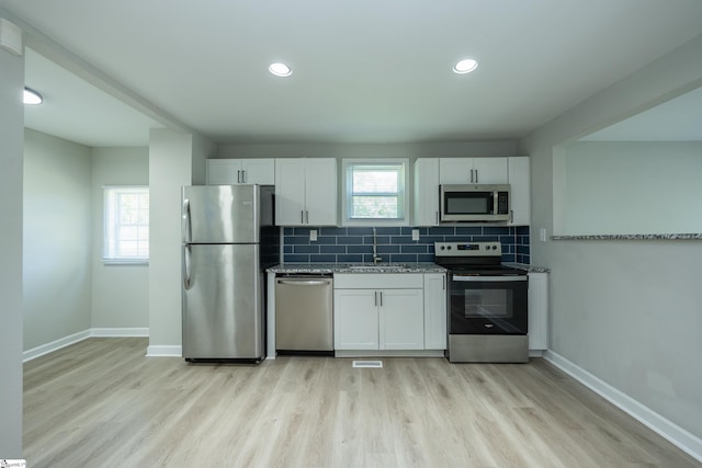 kitchen featuring light wood-style flooring, tasteful backsplash, baseboards, white cabinetry, and appliances with stainless steel finishes