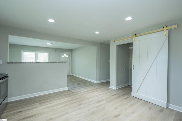 spare room featuring a barn door, baseboards, light wood-style floors, and recessed lighting