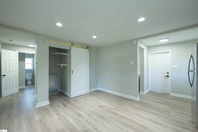 unfurnished bedroom featuring a barn door, recessed lighting, freestanding refrigerator, baseboards, and light wood-style flooring