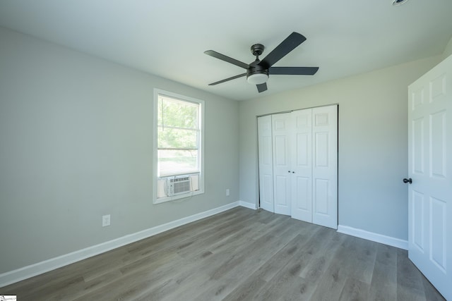 unfurnished bedroom featuring baseboards, wood finished floors, cooling unit, and a closet