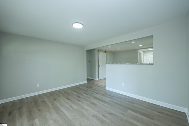 spare room with recessed lighting, a barn door, baseboards, and light wood-style flooring