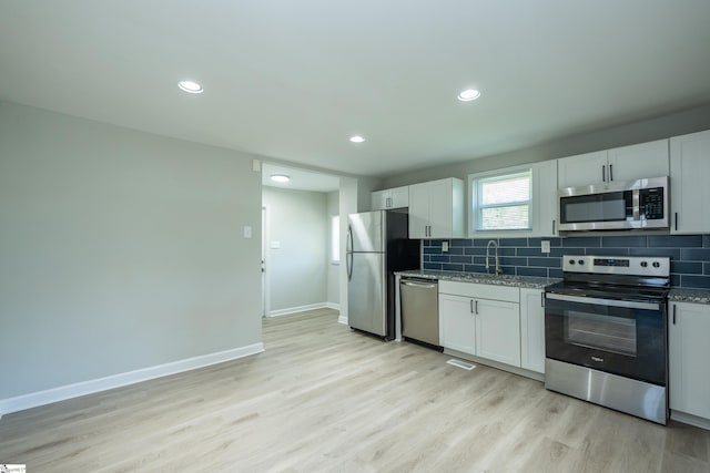kitchen with light wood-type flooring, stone counters, baseboards, backsplash, and appliances with stainless steel finishes