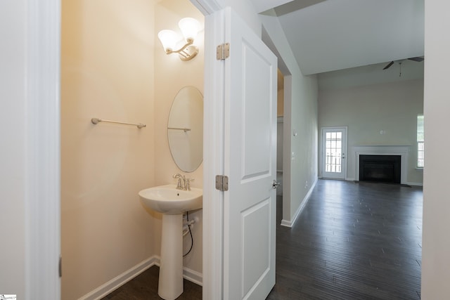 bathroom with a sink, wood finished floors, ceiling fan, a fireplace, and baseboards