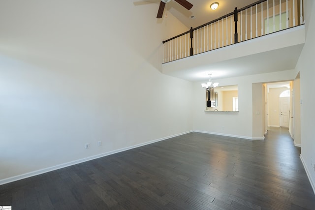 unfurnished living room featuring baseboards, a high ceiling, dark wood-style floors, and ceiling fan with notable chandelier