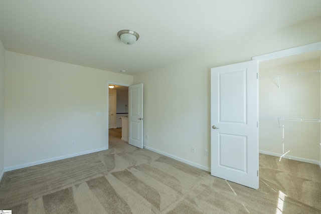 unfurnished bedroom with light colored carpet, baseboards, a spacious closet, and a closet