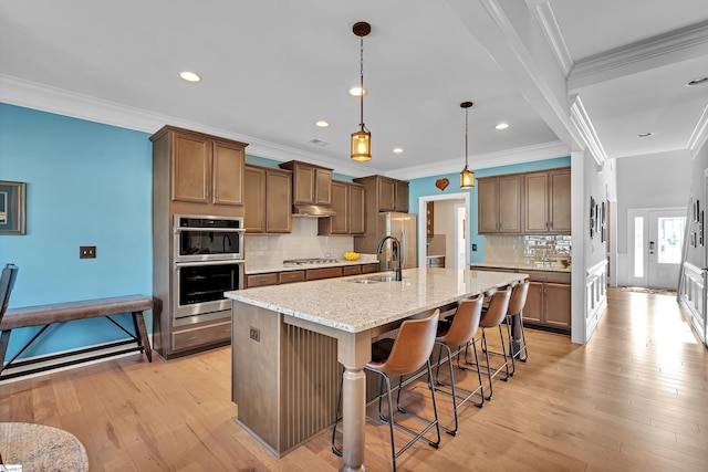 kitchen featuring light wood-style flooring, a sink, light stone countertops, a breakfast bar, and appliances with stainless steel finishes