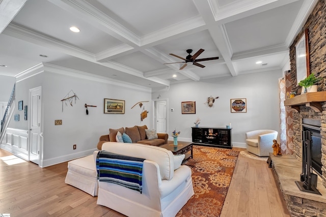living room with light wood-style floors, coffered ceiling, beamed ceiling, ceiling fan, and a stone fireplace