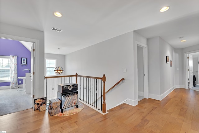 hallway with visible vents, an upstairs landing, light wood-style floors, baseboards, and a notable chandelier