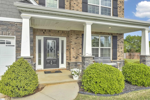doorway to property featuring a porch, fence, and stone siding