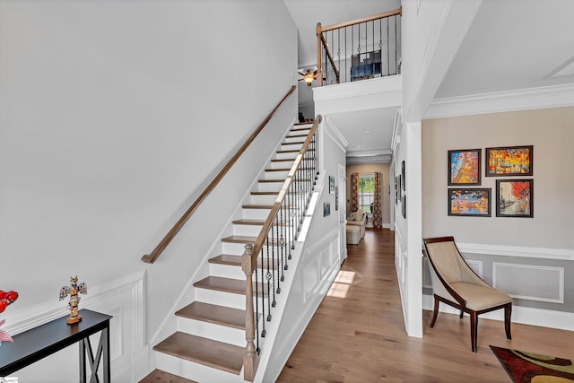 stairway featuring a wainscoted wall, wood finished floors, a decorative wall, and crown molding