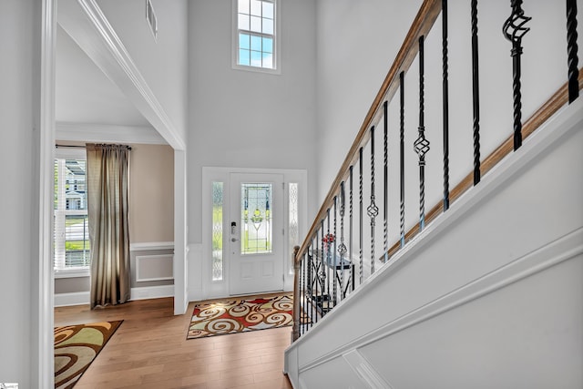 entryway featuring stairway, a high ceiling, visible vents, wood-type flooring, and wainscoting
