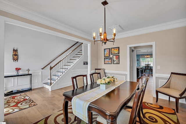 dining room featuring stairway, a wainscoted wall, an inviting chandelier, crown molding, and light wood-style flooring