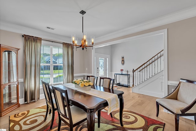 dining space with light wood finished floors, visible vents, an inviting chandelier, stairs, and ornamental molding