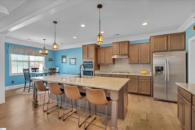 kitchen with a kitchen breakfast bar, a sink, appliances with stainless steel finishes, light wood finished floors, and under cabinet range hood