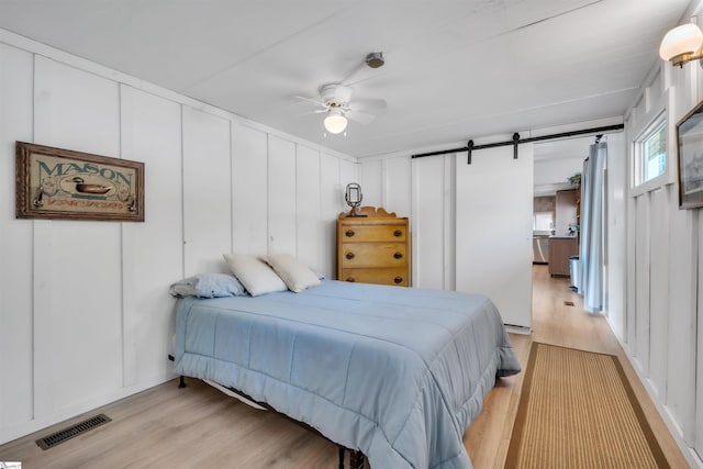 1506 W Lakeshore Dr, Landrum, SC 29356 - bedroom with a barn door, a decorative wall, light wood-style floors, ceiling fan, and visible vents
