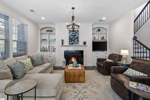 living room with stairway, a glass covered fireplace, a chandelier, built in shelves, and visible vents